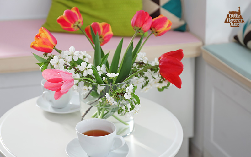 Pink tulips in a vase and two cups of tea on a white table
