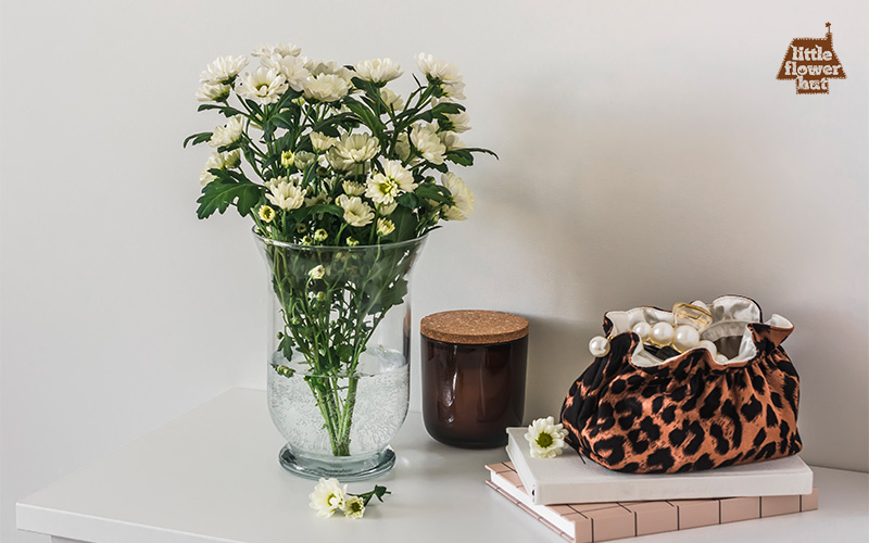White daisies in a glass vase with decorative accessories beside