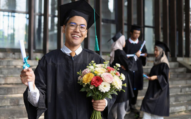 Male graduate holding a diploma and colorful graduation flowers.