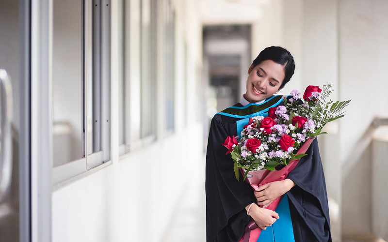 Smiling graduate holding a large bouquet of red roses.