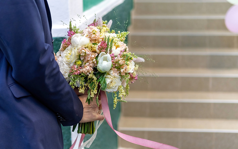 Man in suit holding graduation flowers to congratulate someone.